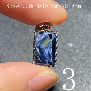Puede incluir: Colgante rectangular con una piedra preciosa azul y dorada, engastada en un marco plateado. La piedra tiene un patrón arremolinado. Mide 9,8 mm x 18,5 mm x 3,2 mm. El número 3 es visible.