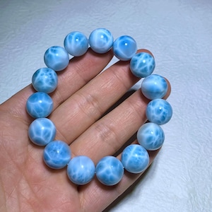May include: A light blue beaded bracelet featuring round, polished beads. The beads have a marbled appearance with white and light blue patterns. The bracelet is a jewelry item, likely worn on the wrist.