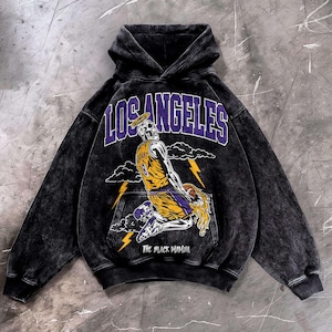 May include: Black hooded sweatshirt with a graphic of a skeleton wearing a basketball jersey with the number 8. The word "LOS ANGELES" is above the skeleton in purple letters. The text "THE BLACK MAMBA" is below the skeleton.