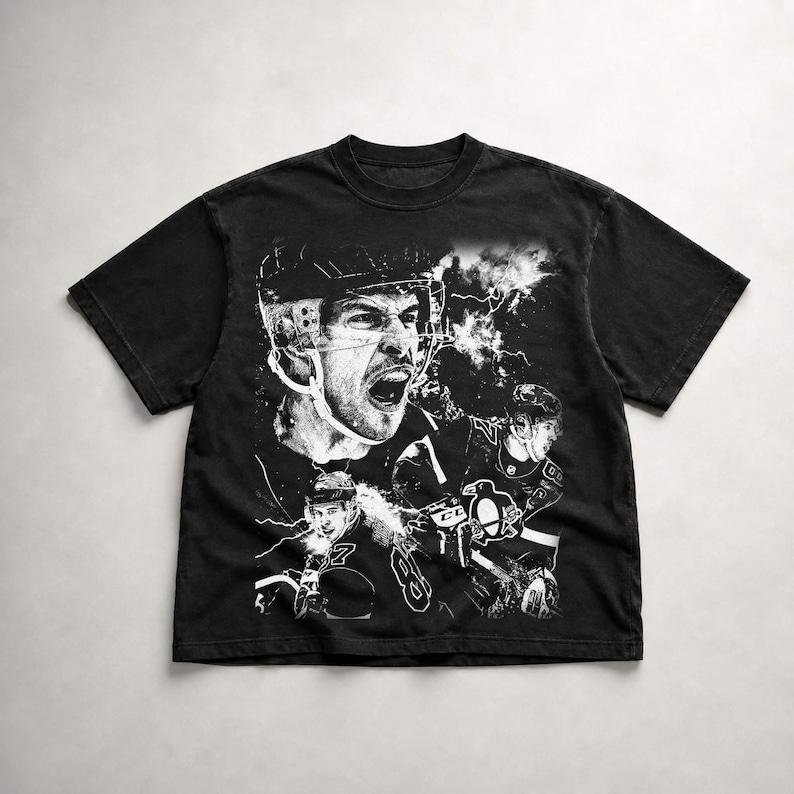 May include: A black short-sleeve t-shirt featuring a large white graphic print of a hockey player in a helmet with an open mouth expression, alongside a smaller player wearing a jersey with a penguin logo and the number 87, set against lightning.