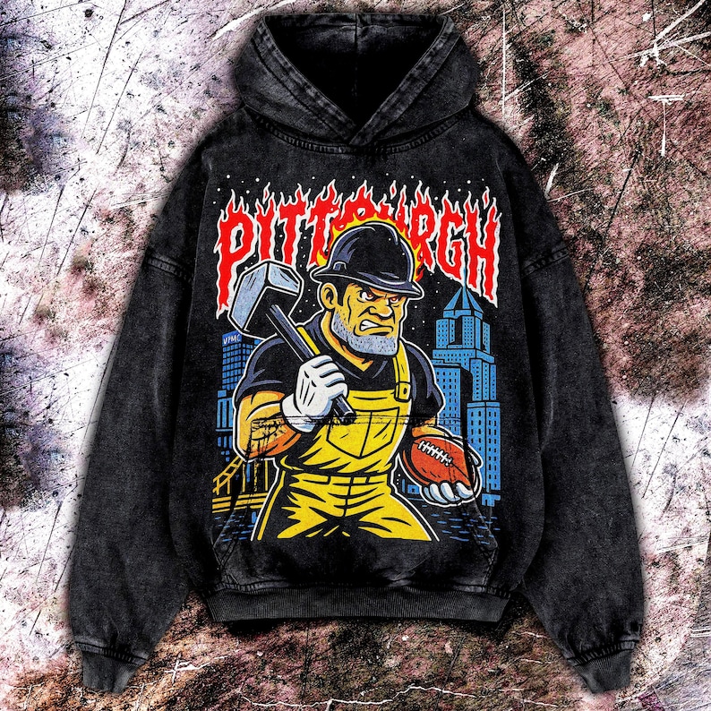 May include: Black hooded sweatshirt with a distressed graphic featuring a construction worker holding a hammer and football, with the word "PITTSBURGH" in flames. The worker wears a hard hat and yellow overalls. The background shows a city skyline.