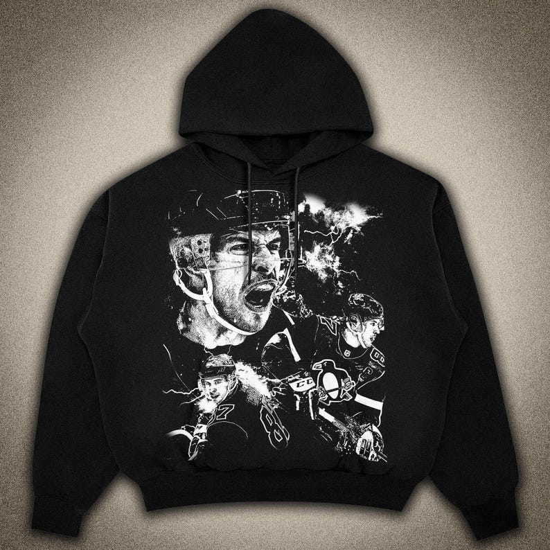 Pode incluir: Hoodie preto com um estampado gr&aacute;fico branco de jogadores de h&oacute;quei vestindo capacetes e uniformes. O gr&aacute;fico inclui o texto "C.B." e um logotipo de pinguim.