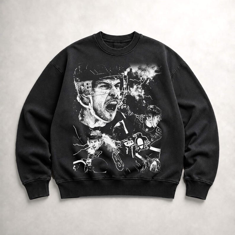 May include: A black crewneck sweatshirt featuring a large, white, high-contrast graphic print of a hockey player in a helmet with an open mouth, alongside a smaller player in a jersey with a penguin logo and the number 87, set against lightning.