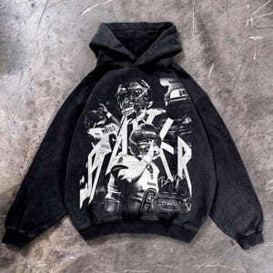 Peut inclure: Sweat à capuche noir avec un motif de joueurs de football américain et le nom "Baker" en blanc. Le vêtement a un aspect vintage et délavé.