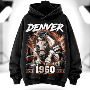 Peut inclure: Un sweat à capuche noir avec un motif représentant un cheval portant un maillot numéro 303 et un bandeau marqué 5280. Le texte indique DENVER, MILE HIGH MENTALITY et 1960 EST. Le design comporte des accents de couleur orange et blanche.