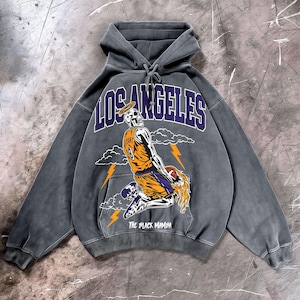 May include: Gray hoodie with a graphic of a skeleton wearing a basketball jersey with the number 18. The word "LOS ANGELES" is arched across the top in purple, and "THE BLACK MAMBA" is printed at the bottom.