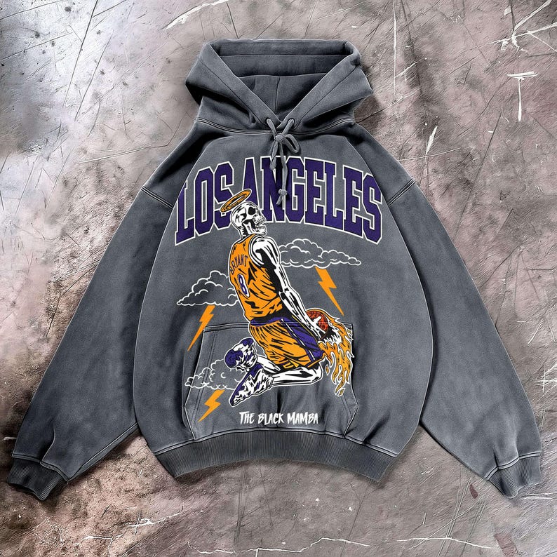 May include: Gray hoodie with a graphic of a skeleton wearing a basketball jersey with the number 18. The word "LOS ANGELES" is arched across the top in purple, and "THE BLACK MAMBA" is printed at the bottom.