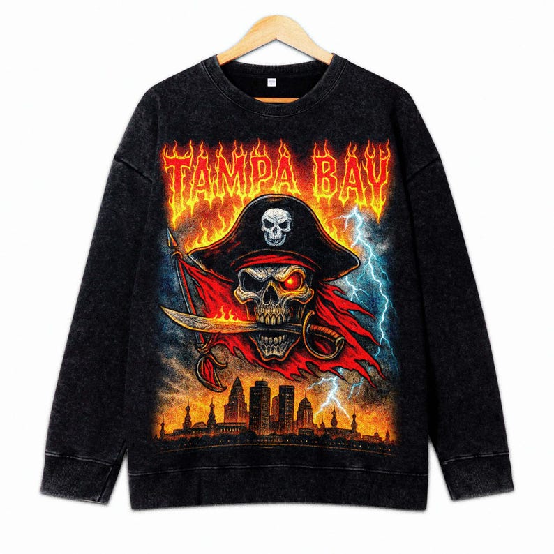 May include: Black sweatshirt with a pirate skull design. The skull wears a hat and bandana, holding a sword. The text "TAMPA BAY" is above the skull in a fiery font. A cityscape is at the bottom with lightning in the background.