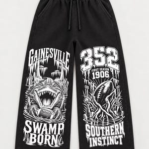 May include: Black sweatpants with an elastic drawstring waistband and wide legs. The front features white graphic prints: the left leg shows an alligator holding a football with the text "GAINESVILLE SWAMP BORN," and the right leg displays a football with "352 FIRST SEASON 1906 SOUTHERN INSTINCT."