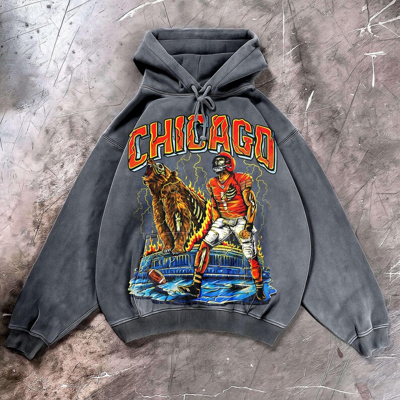 May include: A grey hooded sweatshirt with a graphic of a football player and a bear, and the word "CHICAGO" in orange. The design incorporates lightning and flames, giving it a vintage look.