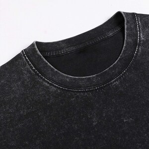 Pode incluir: Uma camiseta preta de gola redonda com um visual desgastado e vintage. O tecido tem uma apar&ecirc;ncia desbotada e desgastada.