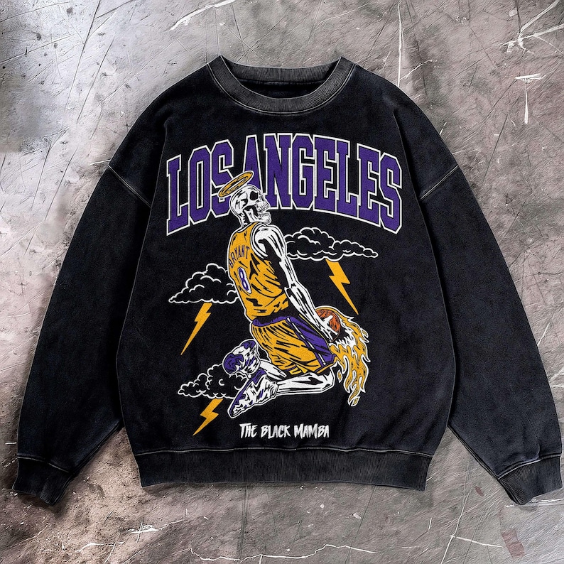 May include: Black crewneck sweatshirt featuring a skeleton wearing a basketball uniform with the number 8. The graphic includes the words "LOS ANGELES" and "THE BLACK MAMBA" in purple and white.