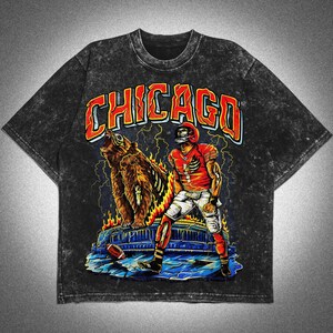 May include: Dark grey acid wash t-shirt with a graphic of a football player and a bear, and the word "CHICAGO" in orange and red. The design includes lightning bolts and flames, with a football on the ground.
