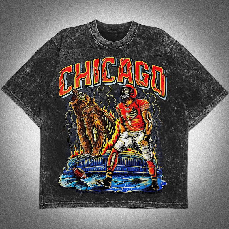 May include: Dark grey acid wash t-shirt with a graphic of a football player and a bear, and the word "CHICAGO" in orange and red. The design includes lightning bolts and flames, with a football on the ground.