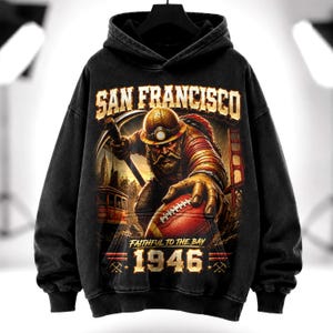 Könnte beinhalten: Ein schwarzer Kapuzenpullover mit einem Grafikdruck eines Bergmanns, der eine Spitzhacke und einen Football hält. Der Text lautet SAN FRANCISCO, FAITHFUL TO THE BAY und 1946. Das Design zeigt eine Seilbahn und die Golden Gate Bridge.