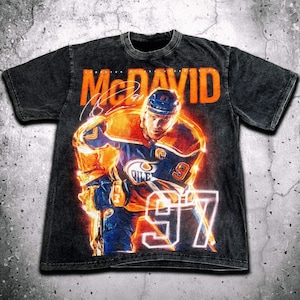 May include: Black t-shirt with a graphic of hockey player Connor McDavid in an orange and blue jersey with the text "McDavid" and "97" in orange.