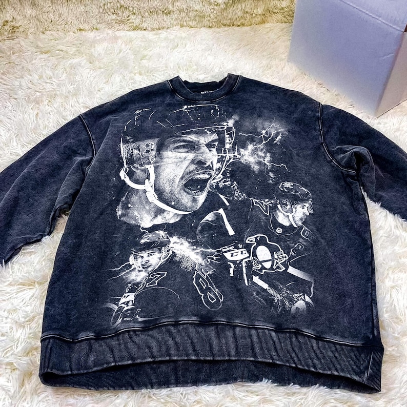 Pode incluir: Camisola de moletom preta com um visual desgastado com uma estampa gr&aacute;fica branca de um jogador de h&oacute;quei vestindo um capacete e o logotipo de um time de h&oacute;quei.
