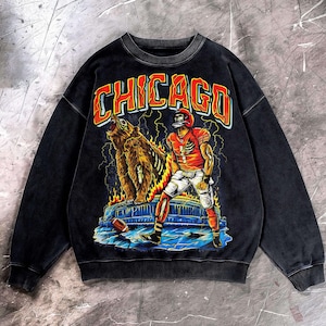 May include: Black crew neck sweatshirt with a distressed graphic. The design features a football player, a bear, and the word "CHICAGO" in orange and red. Includes lightning bolts and flames.