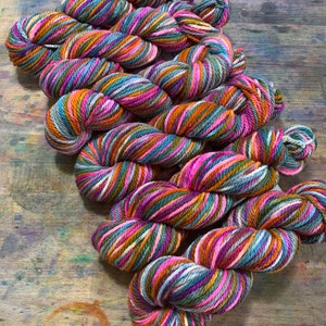 May include: A collection of colorful yarn skeins. The yarn is a mix of pink, orange, teal, and brown, creating a striped pattern. The skeins are arranged on a wooden surface, showcasing the vibrant colors and textures of the yarn.