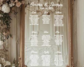May include: A gold-framed mirror with a seating chart for a wedding. The names are listed in white text, organized into nine sections. The wedding date is June 18, 2027. Floral arrangements adorn the top left corner.