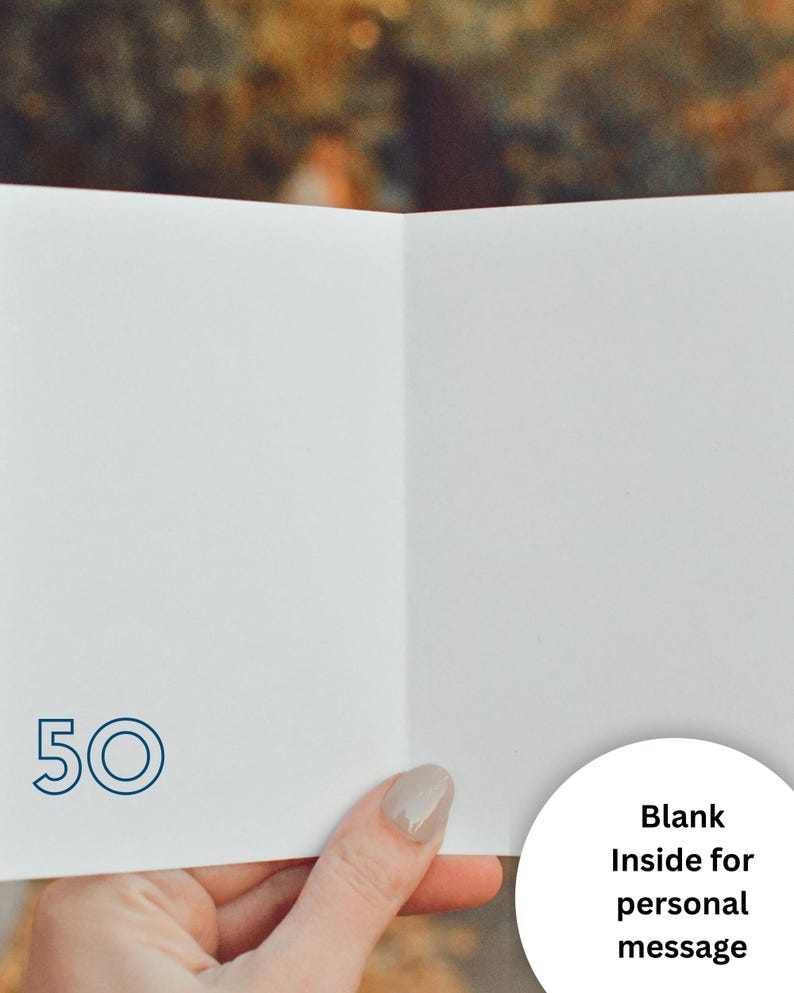 May include: A white greeting card featuring the number 50 printed in a dark blue outline font on the bottom left corner. The interior of the card is blank, providing space for a personal message. The card is held open to display the interior surface.