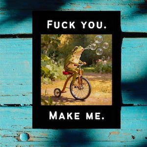 May include: A black rectangular print with the text "FUCK YOU." at the top and "MAKE ME." at the bottom. The image in the center features a frog riding a tricycle and blowing bubbles.