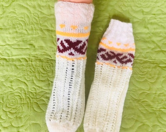 May include: A pair of white knitted socks with a brown and yellow geometric pattern. The socks are on a green background.