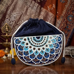 May include: A navy blue drawstring bag with a white and blue decorative pattern. The bag has a white trim and drawstring, with navy blue accents. The bag is on a wooden surface.