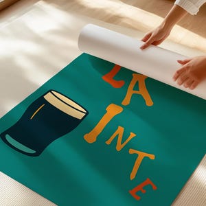 May include: A teal-colored yoga mat with a graphic of a pint of beer and the words "LA PINTE" in orange. The mat is being unrolled by a person. The beer glass is dark blue with a tan rim.