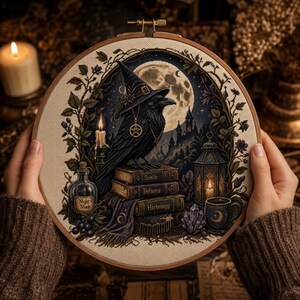 Op de afbeelding: Een ronde borduurring met een kruissteekontwerp van een zwarte raaf met een heksenhoed, zittend op een stapel boeken met de labels Spells, Potions en Herbology, inclusief een volle maan, een lantaarn en een flesje met het label Night Shade.