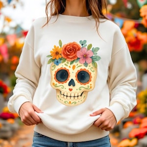 Könnte beinhalten: Cremefarbenes Sweatshirt mit einem bunten Sugar-Skull-Design. Der Totenkopf ist mit Blumen und Mustern verziert, mit großen dunkelblauen Augenhöhlen und einem kleinen Herzen. Das Design ist mittig auf der Vorderseite des langärmeligen Oberteils platziert.
