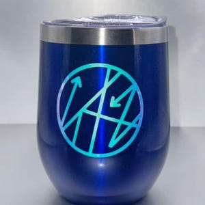 May include: A blue insulated wine tumbler with a silver rim and a clear lid. The tumbler features a teal and blue geometric design inside a circle. The tumbler is designed to keep beverages cold.