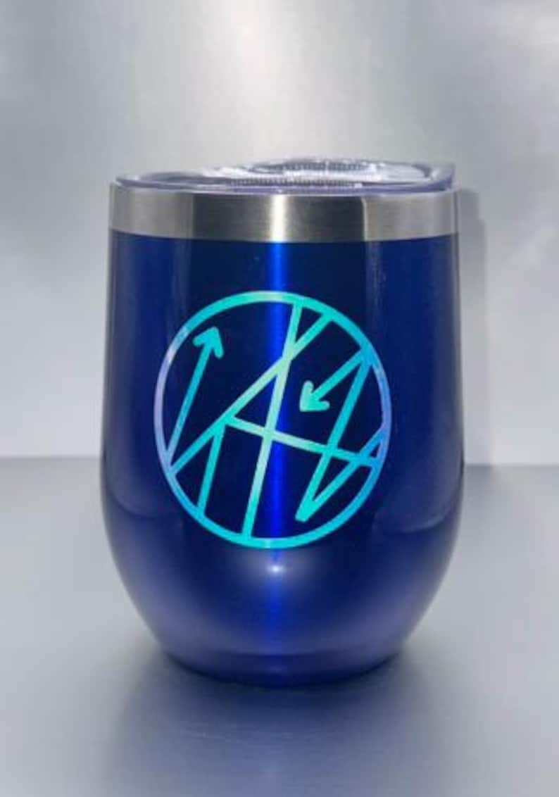 May include: A blue insulated wine tumbler with a silver rim and a clear lid. The tumbler features a teal and blue geometric design inside a circle. The tumbler is designed to keep beverages cold.