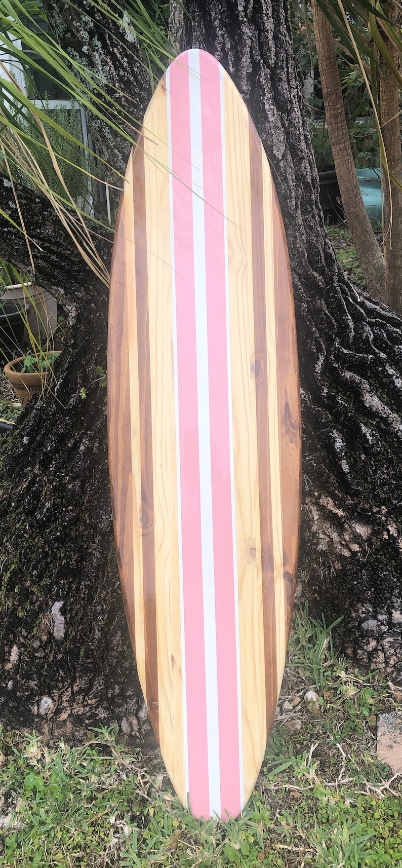 Puede incluir: Una tabla de surf de madera con rayas rosas y blancas. La tabla de surf est&aacute; hecha de diferentes tipos de madera, creando un patr&oacute;n &uacute;nico.