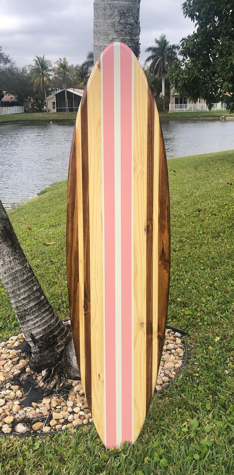 Puede incluir: Una tabla de surf de madera con un dise&ntilde;o de rayas rosas y blancas. La tabla de surf est&aacute; hecha de diferentes tipos de madera, incluyendo madera marr&oacute;n y madera clara.