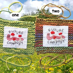 以下が含まれることがあります： 「Future Compost」という文字と、刺繍されたミミズとキノコが描かれた、2つのニット製の壁掛け。壁掛けは緑と茶色で、黄色とオレンジのストライプが入っています。