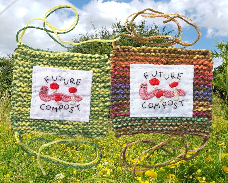 以下が含まれることがあります： ミミズとキノコの刺繍が施されたニットの正方形が2つ。正方形は緑と茶色で、黄色とオレンジのストライプが入っています。正方形のテキストには「Future Compost」と書いてあります。