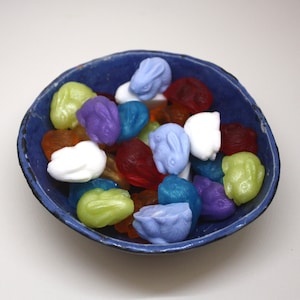 May include: A blue ceramic bowl filled with colorful bunny-shaped candies. The candies are in shades of blue, purple, green, red, white, and yellow.