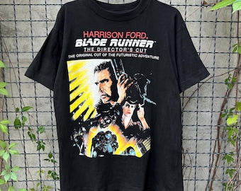 May include: Black t-shirt featuring a movie poster graphic for "Blade Runner." The graphic includes the film's title, "Harrison Ford," and the tagline "The Director's Cut." The image shows a man holding a gun and a woman.