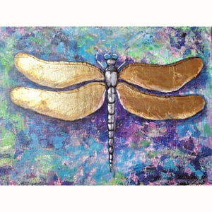 May include: A gold dragonfly with silver wings and body, painted on a blue, green, and purple abstract background. The painting is signed "Nicola 2021" in the bottom right corner.