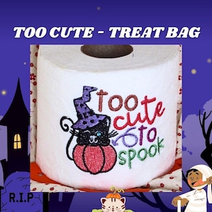 May include: A white toilet paper roll featuring an embroidered design of a black cat wearing a purple witch hat, sitting inside a red pumpkin. The text "too cute to spook" is embroidered in red, purple, and green thread next to the cat.