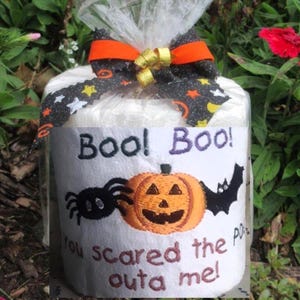 May include: A white toilet paper roll wrapped in clear plastic with an orange and black patterned ribbon bow. The label features an embroidered orange pumpkin, a black spider, a black bat, and the text Boo! Boo! you scared the poop outa me!