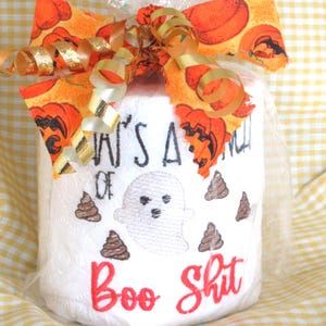 May include: A white toilet paper roll wrapped in clear plastic, topped with an orange fabric bow featuring pumpkin prints and gold ribbons. The roll is embroidered with a ghost, brown poop icons, and the black and red text That's A Bunch Of Boo Shit.