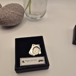 May include: A silver-toned metal pendant shaped like a frog with a floral pattern inside the body, presented in a black jewelry box. A white rectangular label inside the box features the text Fox and Tabby along with small animal silhouettes.