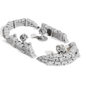 May include: A miniature war game terrain set featuring gray sandbag walls and three miniature figures. The sandbag walls are arranged in curved and straight sections. The figures are in a battle stance, suggesting a war game theme.