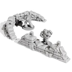 May include: A miniature gray battlefield scene featuring two armored figures and sandbag fortifications. The sandbags are arranged in curved and straight lines, creating defensive positions. The figures are standing on circular bases.