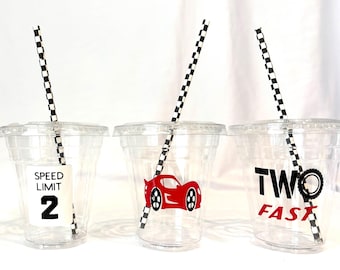 May include: Four clear plastic cups with lids and black and white checkered straws. Each cup has a different racing-themed design: checkered flags, "SPEED LIMIT 2", a red race car, and "TWO FAST" with a tire graphic.
