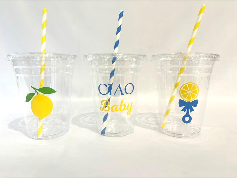 May include: Three clear plastic cups with lids and straws. Each cup has a different design: a lemon, the text "CIAO Baby", and a lemon rattle. The straws are yellow and white or blue and white striped.