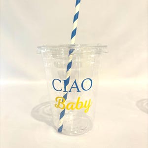 May include: A clear plastic cup with a lid and a blue and white striped straw. The cup has the words "CIAO Baby" printed on it in blue and yellow. The cup is designed for cold beverages.