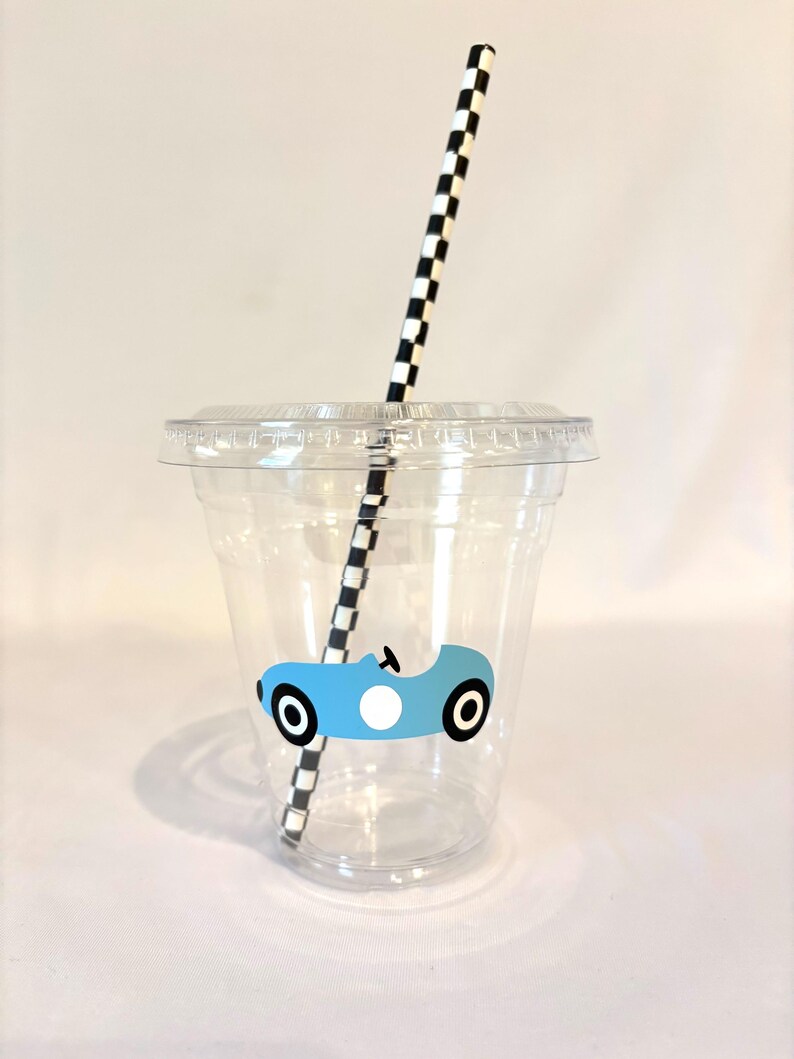 Puede incluir: Un vaso de pl&aacute;stico transparente con tapa y pajita a cuadros blancos y negros. El vaso tiene un gr&aacute;fico de coche de carreras azul claro. Para bebidas fr&iacute;as.
